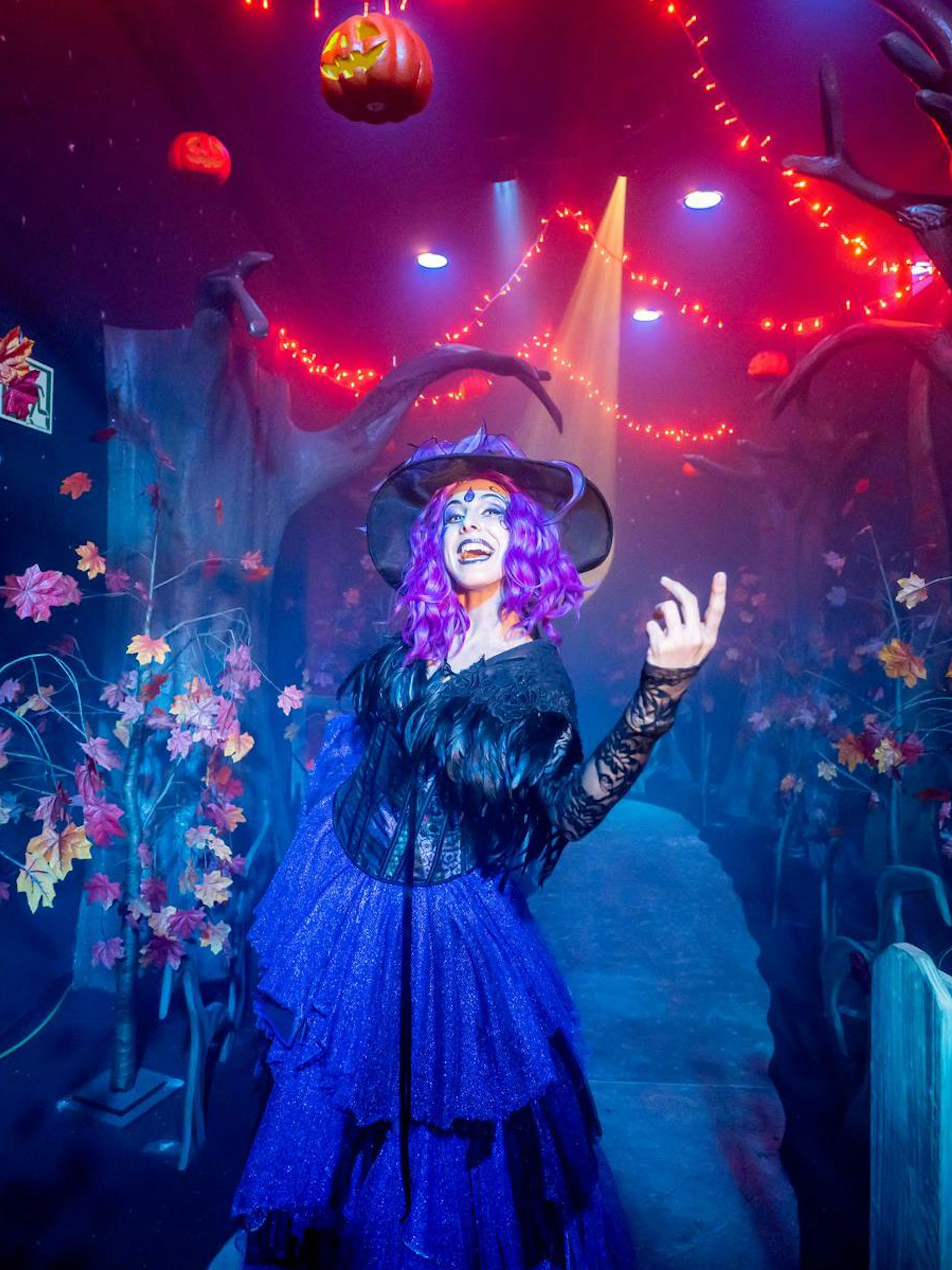 Witch in costume at PortAventura Park Halloween event with spooky forest decor.