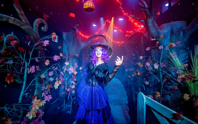 Witch in costume at PortAventura Park Halloween event with spooky forest decor.