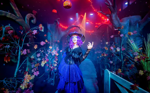 Witch in costume at PortAventura Park Halloween event with spooky forest decor.