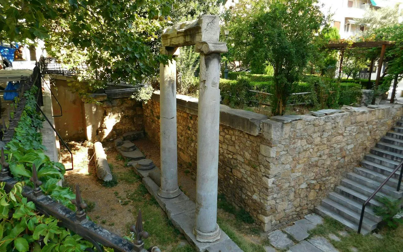 Ancient stone columns and ruins in Plaka, Athens, surrounded by greenery.