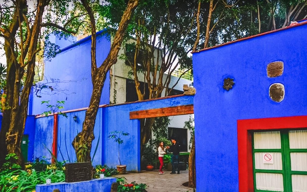 Frida Kahlo Museum courtyard with vibrant blue walls and lush greenery, Mexico City.