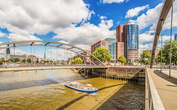 Boat cruising under bridge in Hamburg harbor with cityscape in background.
