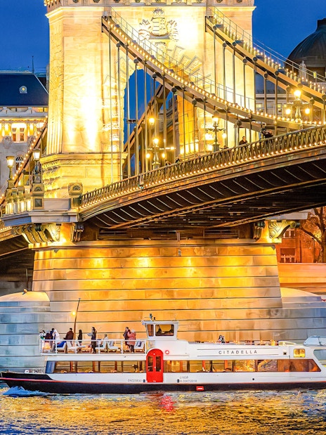Sightseeing cruise boat under illuminated bridge in Budapest at night.