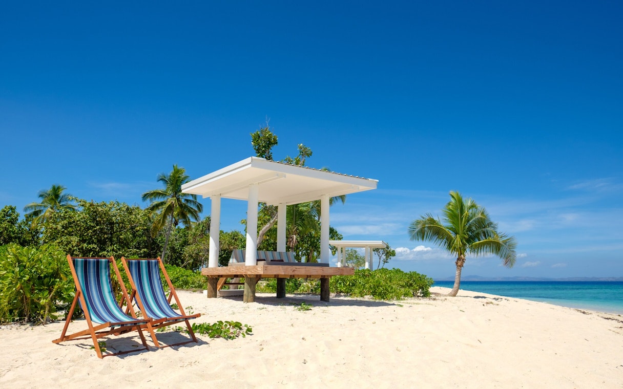 Lounge chairs on sandy beach with cabana and palm trees at Malamala Beach Club, Fiji.