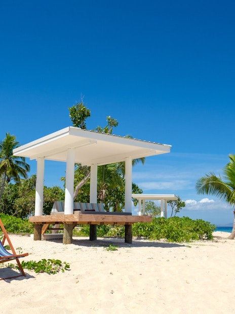 Lounge chairs on sandy beach with cabana and palm trees at Malamala Beach Club, Fiji.