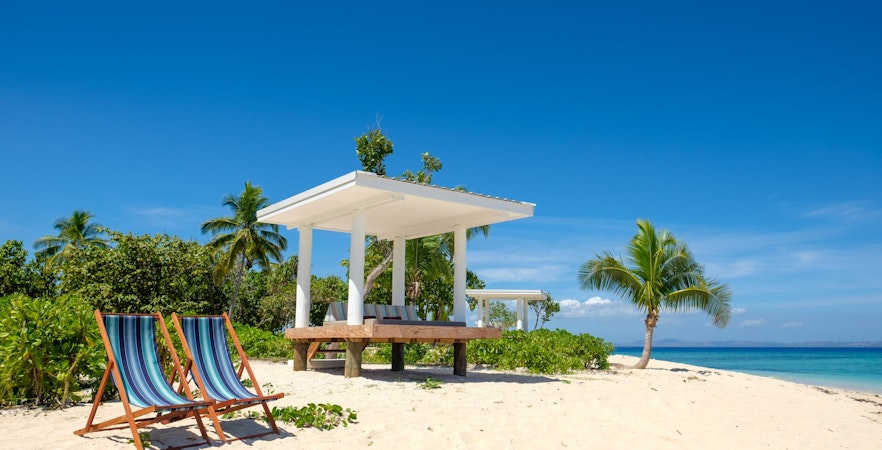 Lounge chairs on sandy beach with cabana and palm trees at Malamala Beach Club, Fiji.