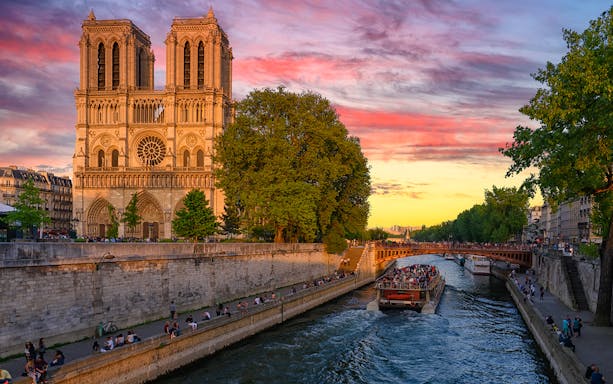 Sunset view of Notre Dame Cathedral in Paris with a boat on the Seine River.