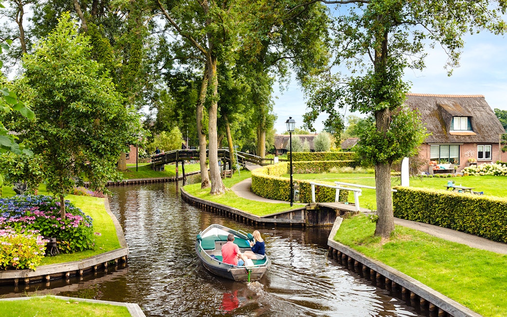 Small electric boat on Giethoorn canal with lush greenery and traditional house.