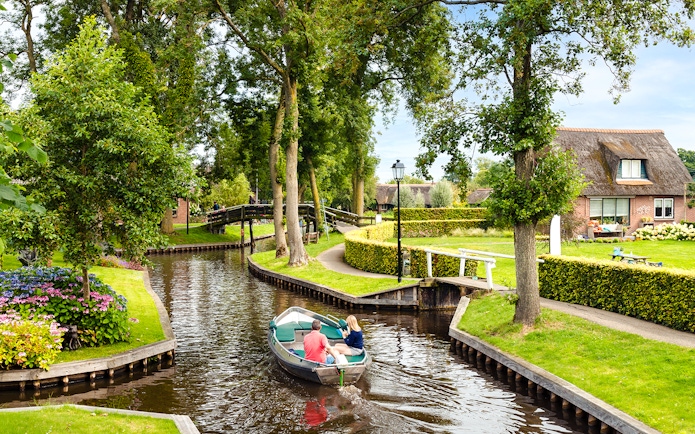 Small electric boat on Giethoorn canal with lush greenery and traditional house.