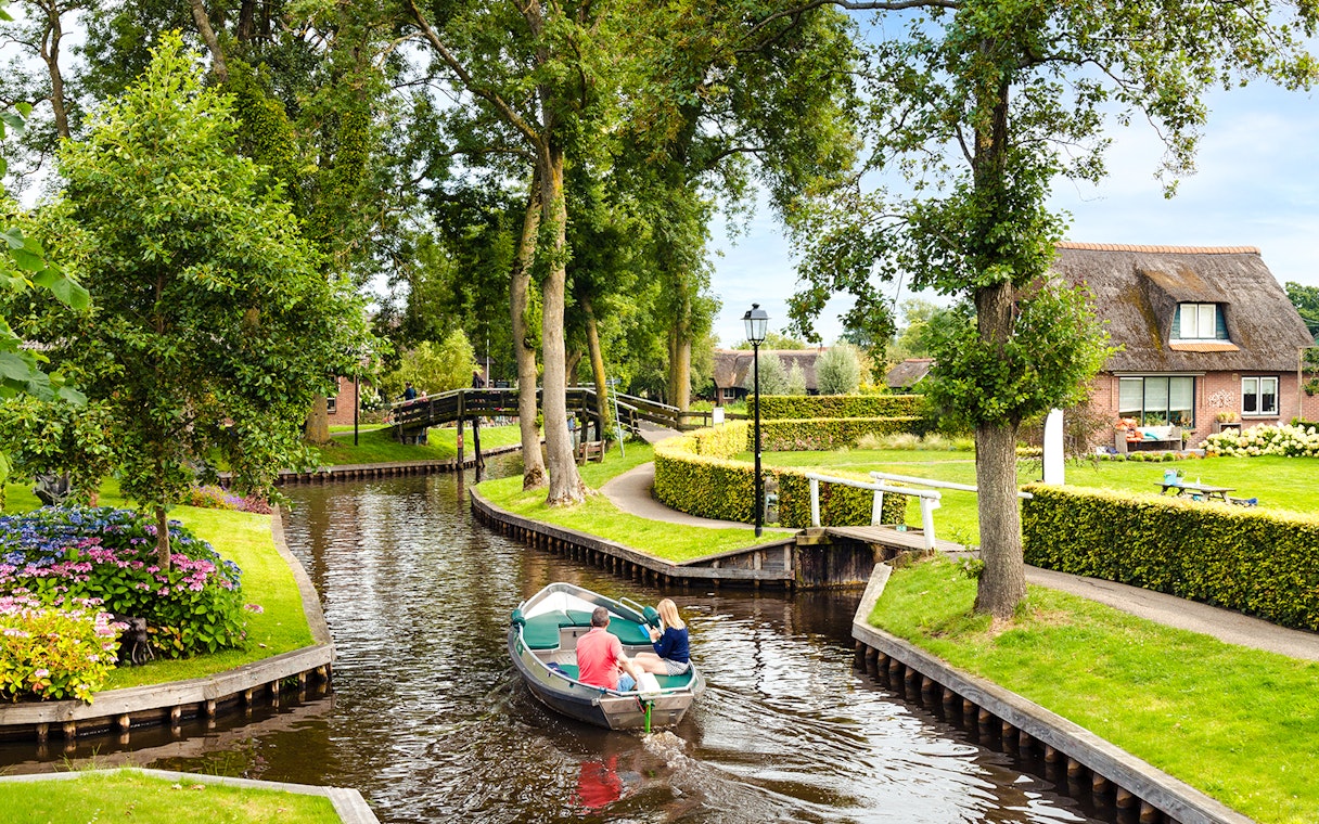 Small electric boat on Giethoorn canal with lush greenery and traditional house.