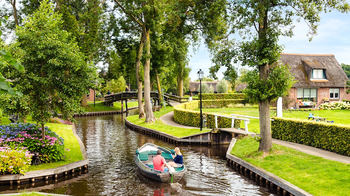 Small electric boat on Giethoorn canal with lush greenery and traditional house.