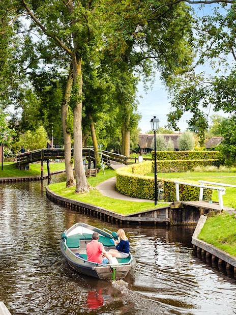 Small electric boat on Giethoorn canal with lush greenery and traditional house.