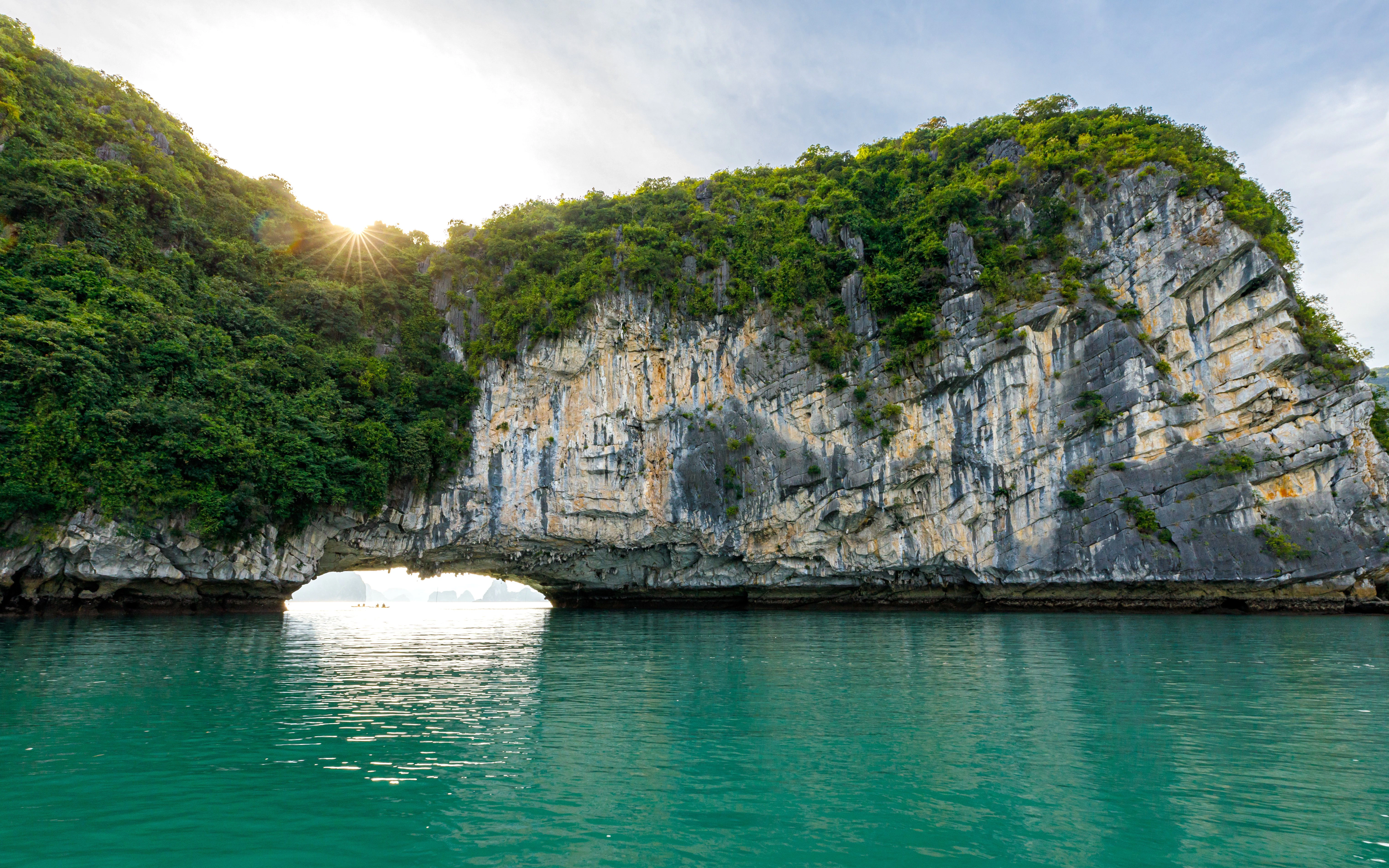 Luon Cave entrance with limestone cliffs and green water in Ha Long Bay, Vietnam.