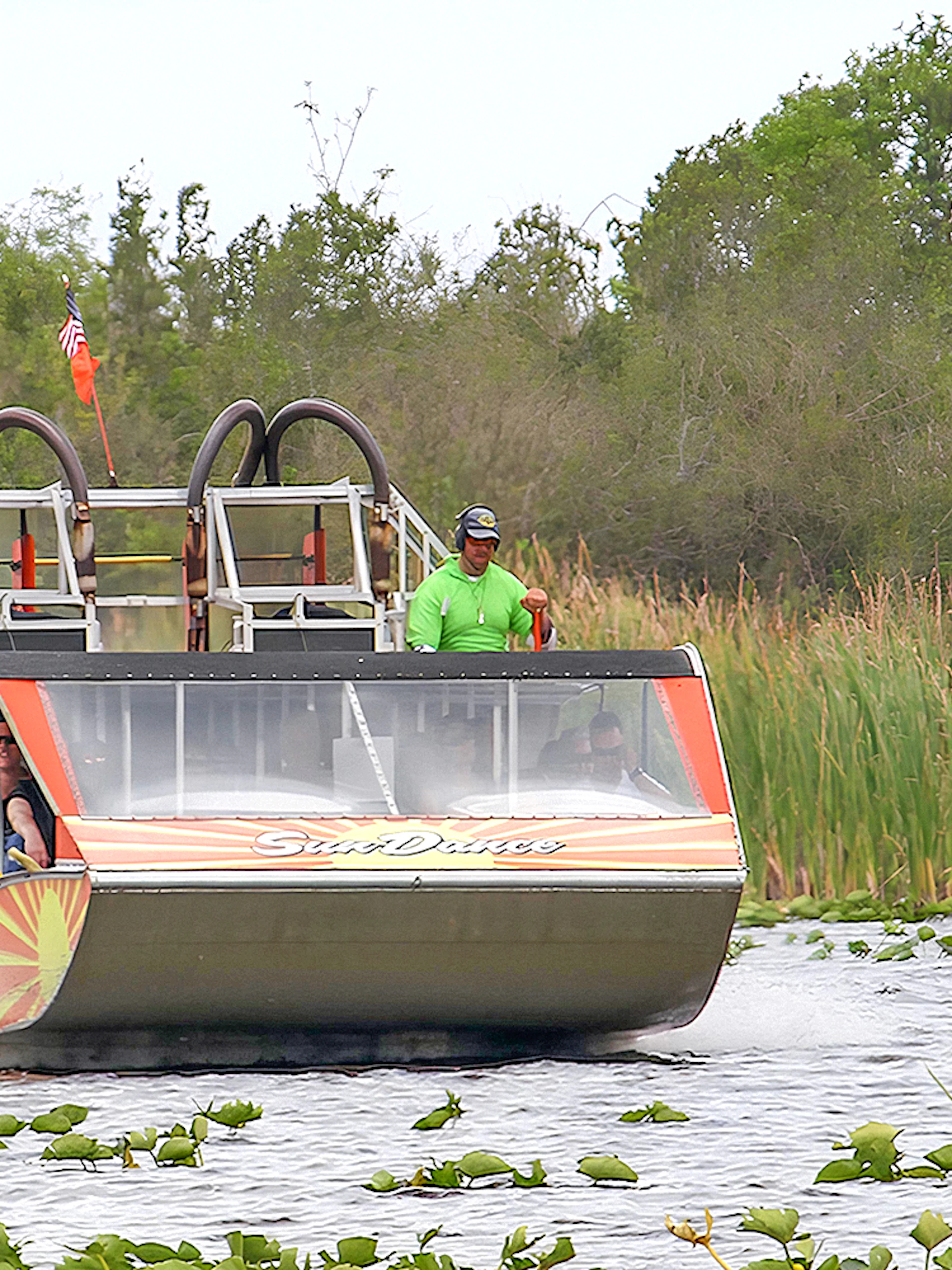 Airboat gliding through Everglades National Park with passengers, surrounded by lush greenery.