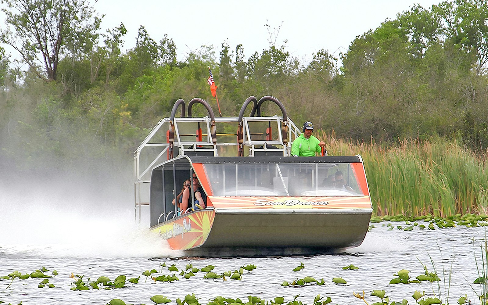 Airboat gliding through Everglades National Park with passengers, surrounded by lush greenery.
