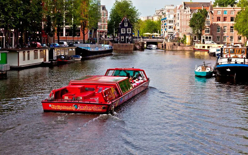 City Sightseeing Amsterdam boat cruising through canal with historic buildings.