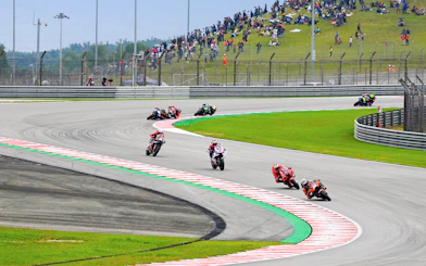 Motorcycles racing on track at Petronas Grand Prix of Malaysia 2023 with spectators on hillside.