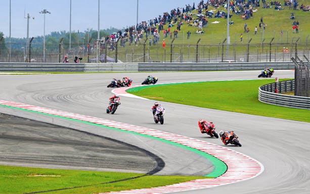 Motorcycles racing on track at Petronas Grand Prix of Malaysia 2023 with spectators on hillside.