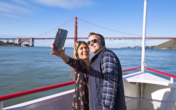 Couple photographing Golden Gate Bridge from Bay Cruise, San Francisco, USA.