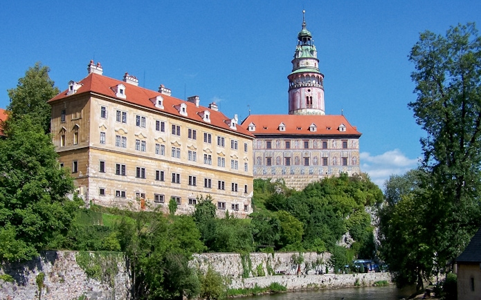 Cesky Krumlov Castle with red roofs and tower, surrounded by greenery.