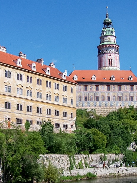 Cesky Krumlov Castle with red roofs and tower, surrounded by greenery.