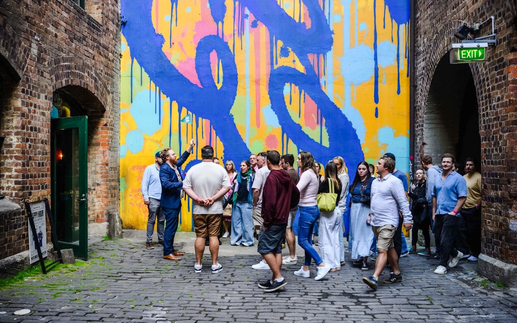 Group of people in front of colorful mural at Sydney Comedy Festival.