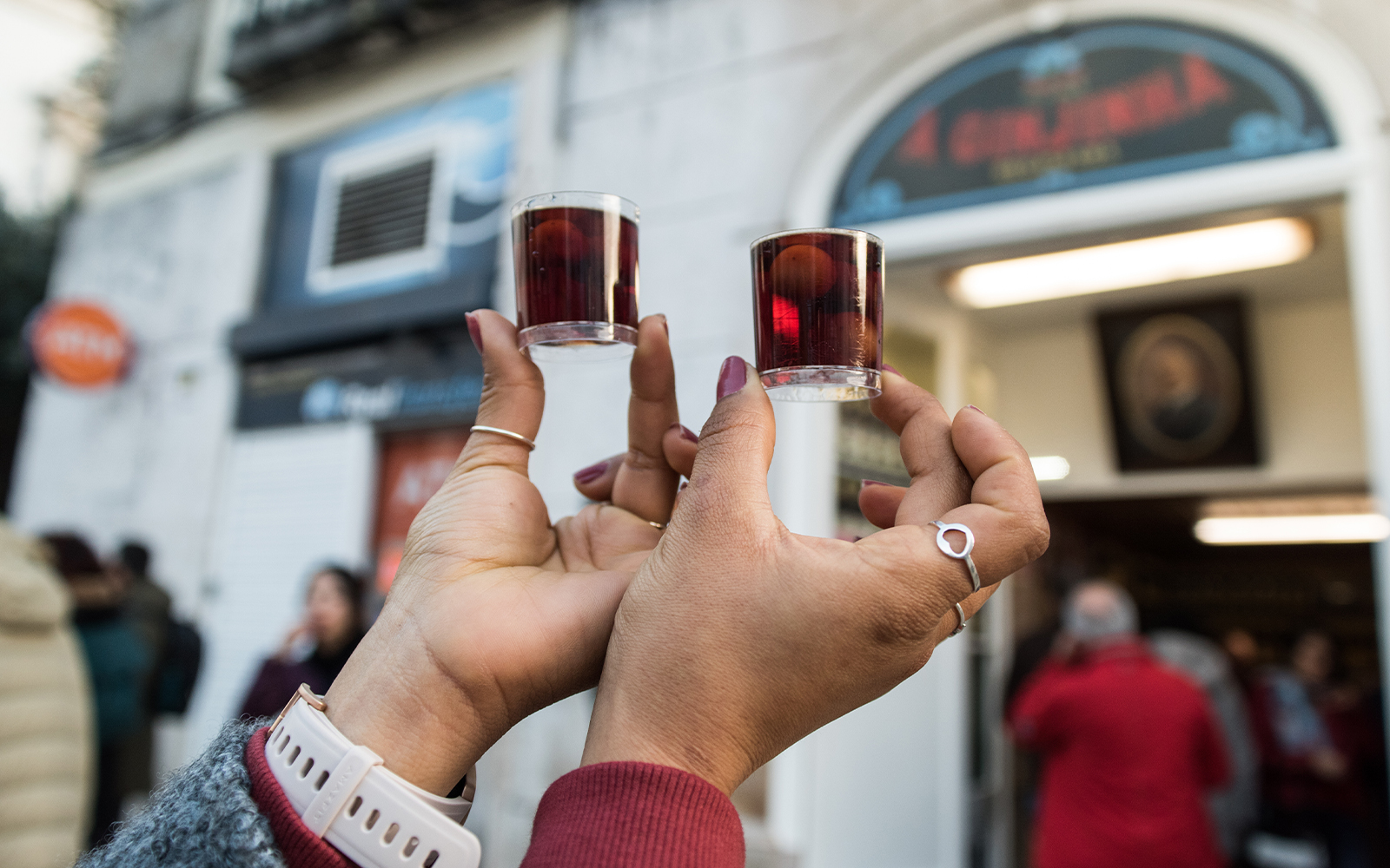 Tourist holding Ginjinha cherry liqueur shots outside Lisbon shop.