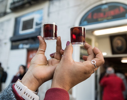 Tourist holding Ginjinha cherry liqueur shots outside Lisbon shop.