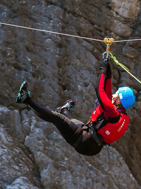 Coasteering participant ziplining over rocky terrain.