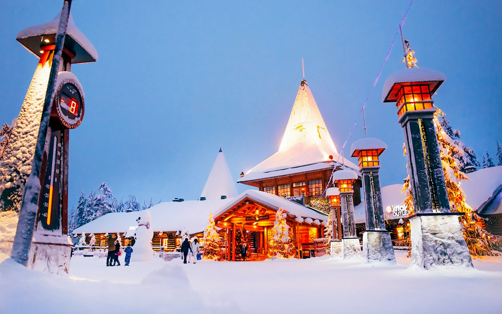 Santa Claus Village entrance in snowy Rovaniemi with visitors and festive lights.