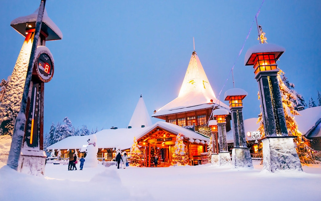 Santa Claus Village entrance in snowy Rovaniemi with visitors and festive lights.