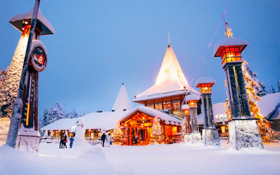 Santa Claus Village entrance in snowy Rovaniemi with visitors and festive lights.
