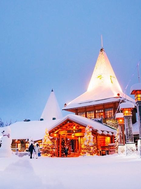 Santa Claus Village entrance in snowy Rovaniemi with visitors and festive lights.
