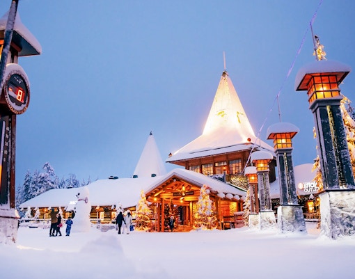 Santa Claus Village entrance in snowy Rovaniemi with visitors and festive lights.