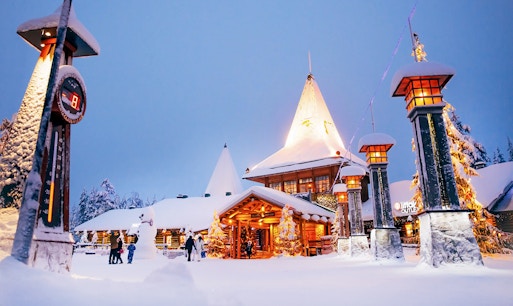 Santa Claus Village entrance in snowy Rovaniemi with visitors and festive lights.