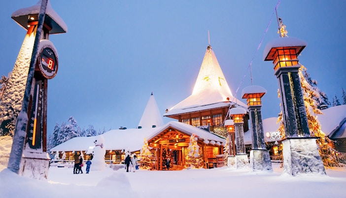 Santa Claus Village entrance in snowy Rovaniemi with visitors and festive lights.