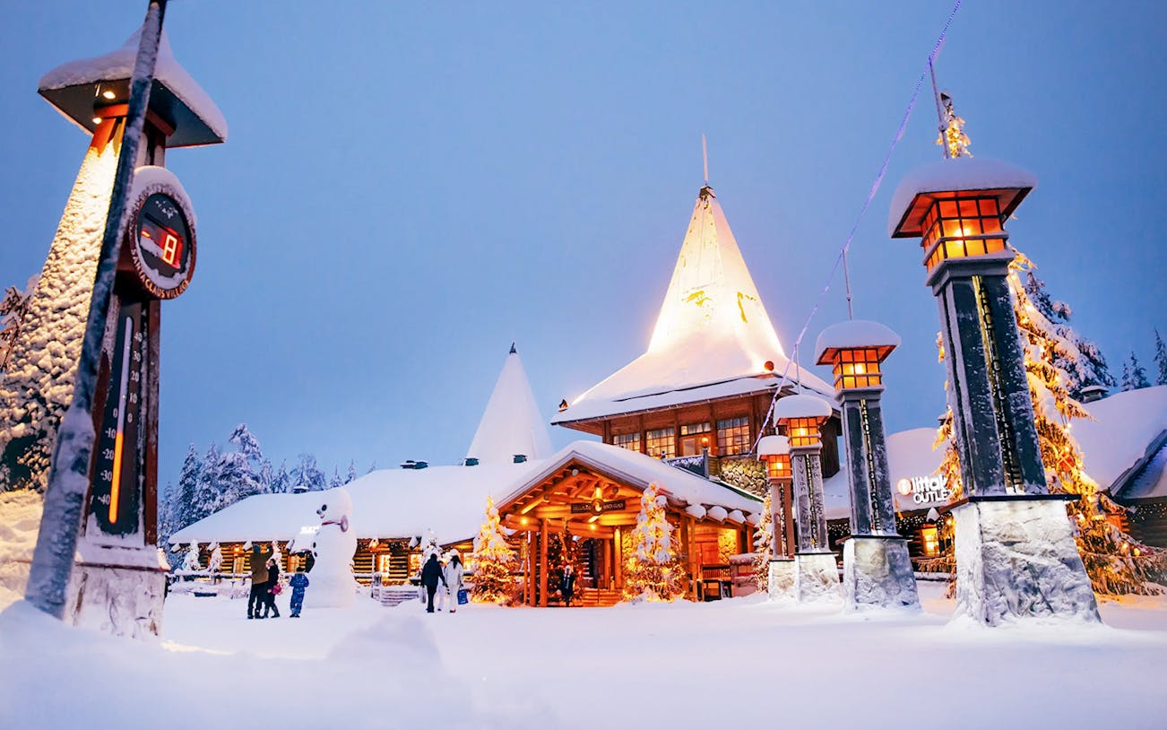 Santa Claus Village entrance in snowy Rovaniemi with visitors and festive lights.
