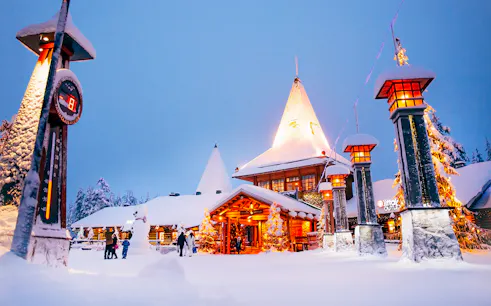 Santa Claus Village entrance in snowy Rovaniemi with visitors and festive lights.