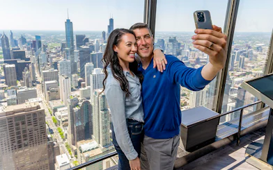 Couple taking a selfie at Chicago 360 Observation Deck with city skyline view.