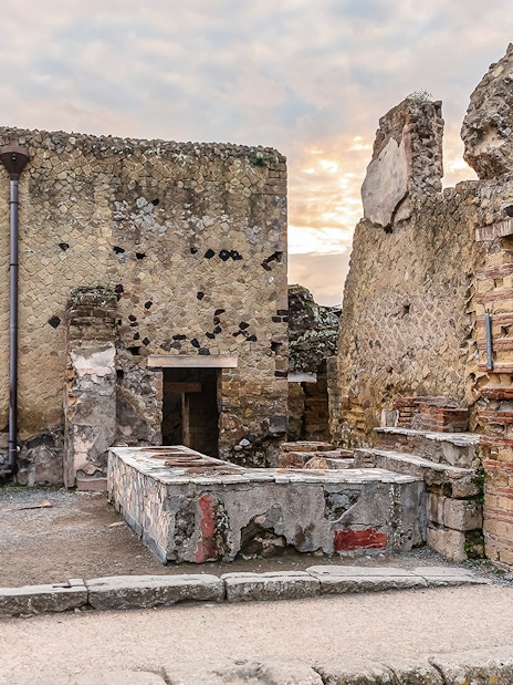 Ancient thermopolium ruins in Herculaneum with stone counters and walls.