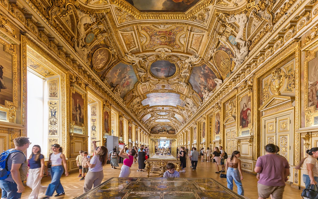 Visitors exploring the ornate Galerie d'Apollon at the Louvre Museum, Paris.