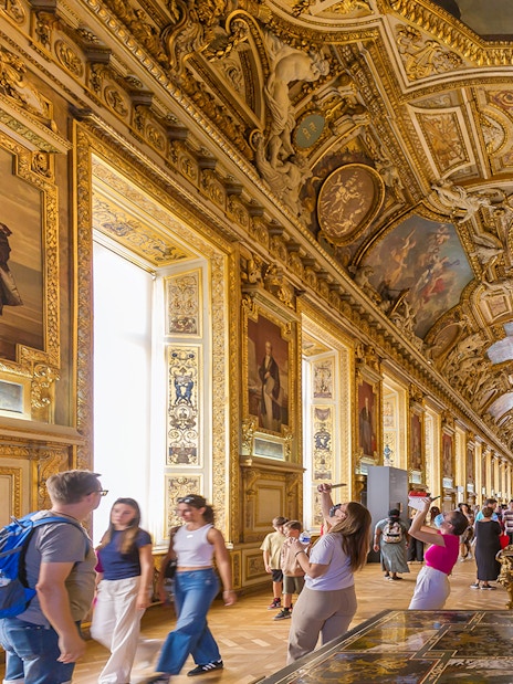 Visitors exploring the ornate Galerie d'Apollon at the Louvre Museum, Paris.