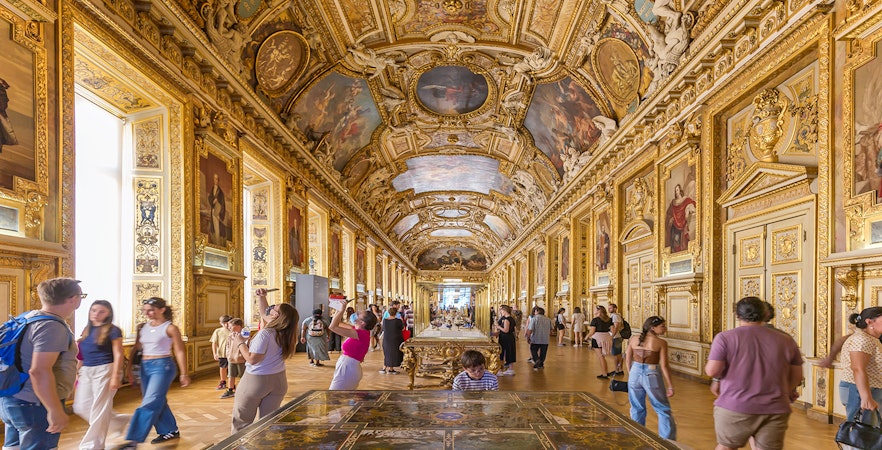 Visitors exploring the ornate Galerie d'Apollon at the Louvre Museum, Paris.