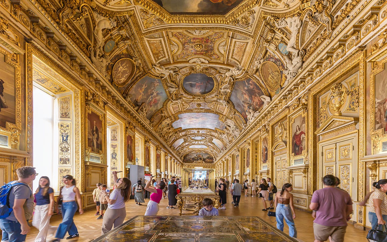 Visitors exploring the ornate Galerie d'Apollon at the Louvre Museum, Paris.