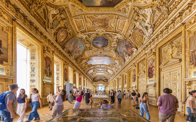 Visitors exploring the ornate Galerie d'Apollon at the Louvre Museum, Paris.