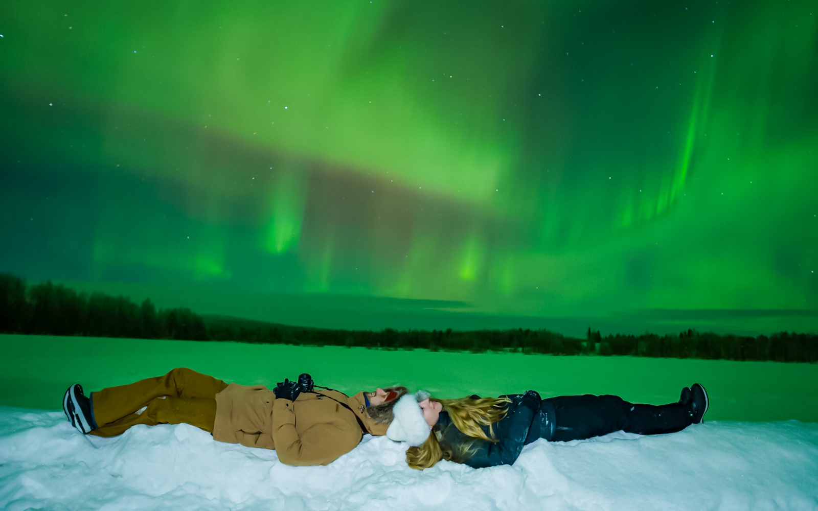 Couple lying on snow watching Northern Lights in Rovaniemi.