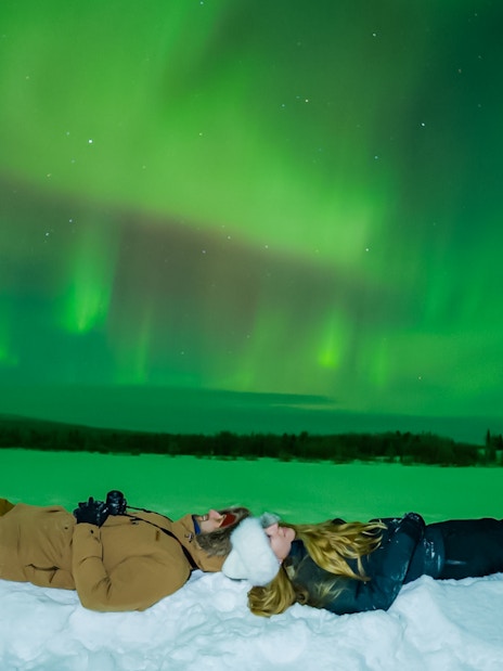 Couple lying on snow watching Northern Lights in Rovaniemi.