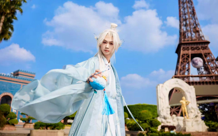 Person in white hanfu with white hair in front of miniature Eiffel Tower.