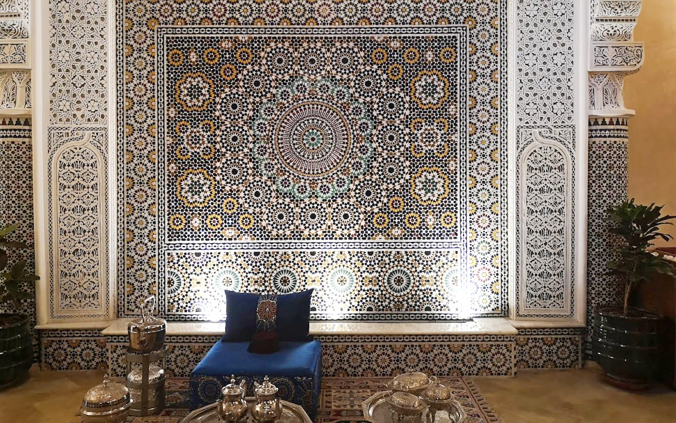 Intricate Moroccan mosaic wall in Marrakech souk with traditional seating and tea set.