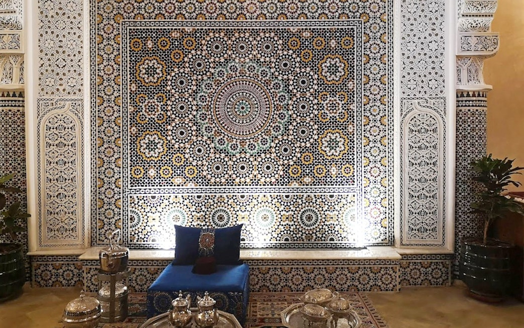 Intricate Moroccan mosaic wall in Marrakech souk with traditional seating and tea set.